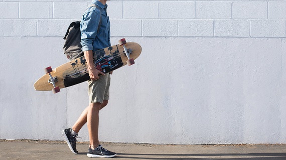 picture of a male with a bag on his back and a skateboard in his arms walking on a sidewalk 