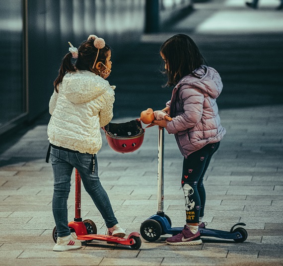 picture of two little girls riding kids scooter outside 