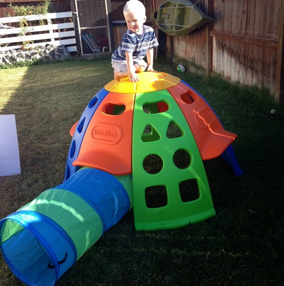 picture of a kid on a play tunnel and climbing dome in a yard on grass  