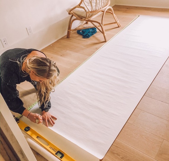 woman measuring glasscloth wallpaper on floor 
