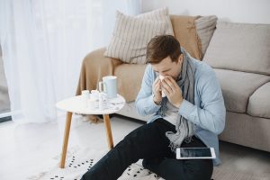 picture of a men sitting beside a bed and coffee table wiping his nose