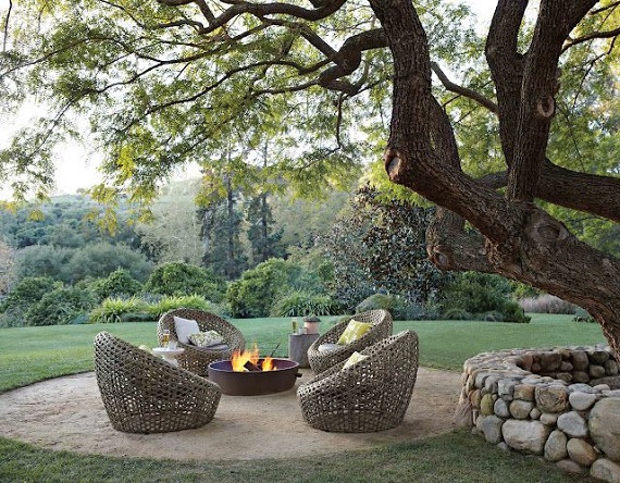 garden chairs around lit fire pit under a tree 