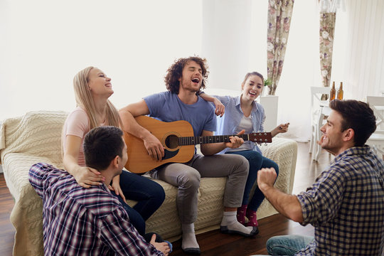 Friends gathered around guy who is playing guitar