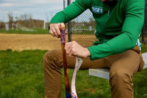 baseball player taping his baseball bat while sitting on a bench