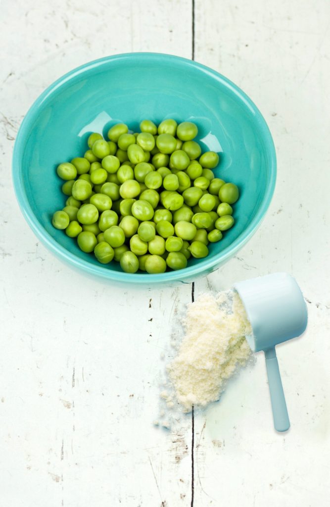 a blue bowl full of peas and a scoop of plant protein powder poured over a table