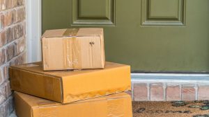 Three cardboard packages stacked on a doorstep in front of a green door, indicating a home delivery.