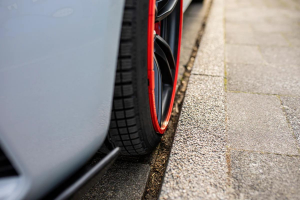 A car wheel with a red alloy protector parked closely to a curb.