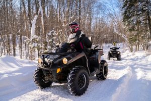 ATV riders navigating a snowy forest trail.