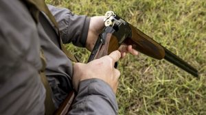 A person loading a double-barrel shotgun with two shells, standing on grassy terrain.