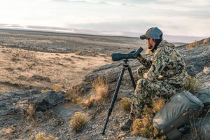 a hunter using a spotting scope in a vast landscape